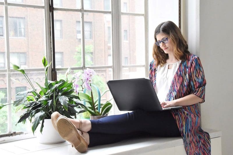 Woman on a computer near a window.