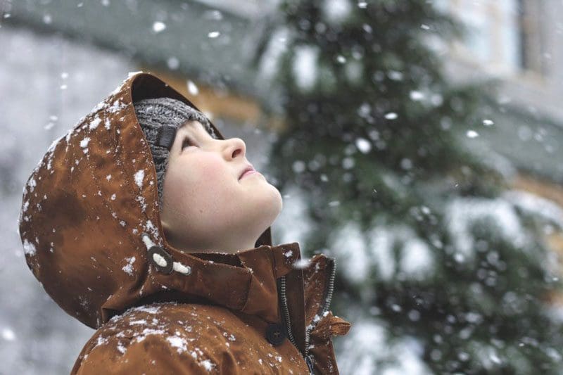 Kid in the snow looking up at the sky.