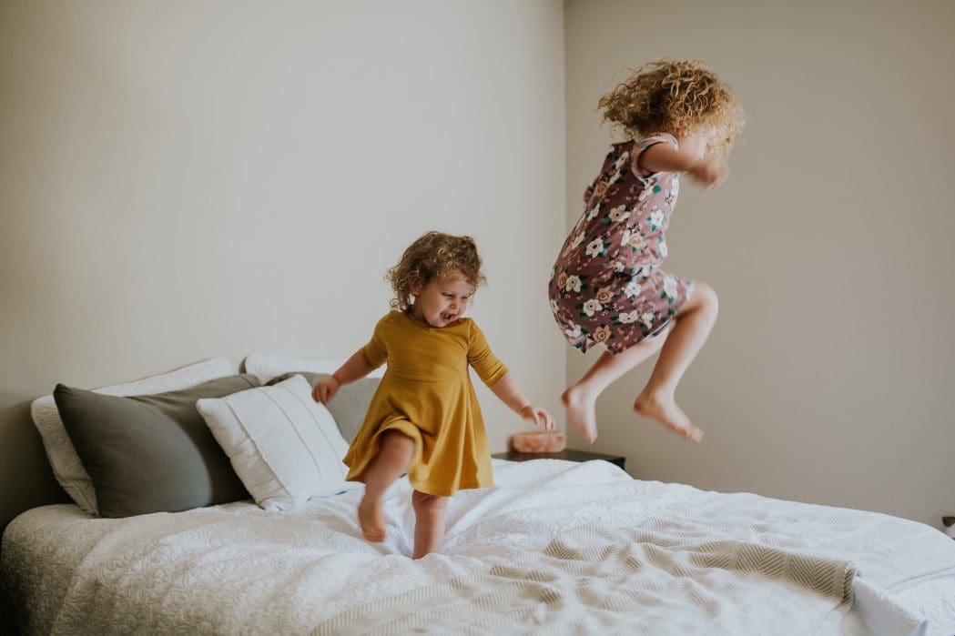 Two small children siblings jumping on the bed