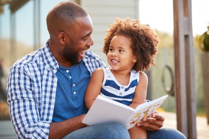 Young father and daughter reading a book outdoors