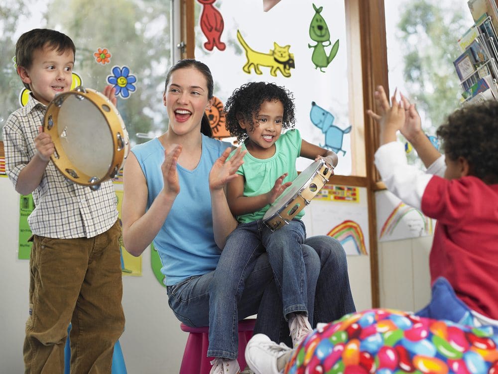 Kids playing with tambourines with their teacher in a classroom